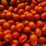 A bountiful harvest of fresh cherry tomatoes ready for use in salads, sauces, or simply enjoyed as a healthy snack. A close-up shot of a stainless steel mixing bowl filled to the brim with small, red and orange cherry tomatoes. The smooth, reflective surface of the bowl contrasts with the natural texture of the tomatoes.